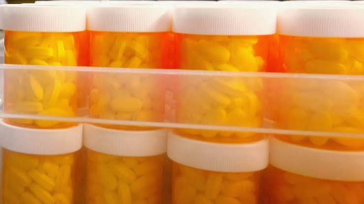 A clear view of a prescription medication bottle sitting on a medical counter next to a hospital facility sign.