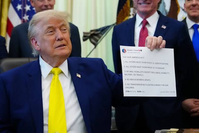 President Donald Trump holding a printed copy of a Truth Social post during an event in the Oval Office.