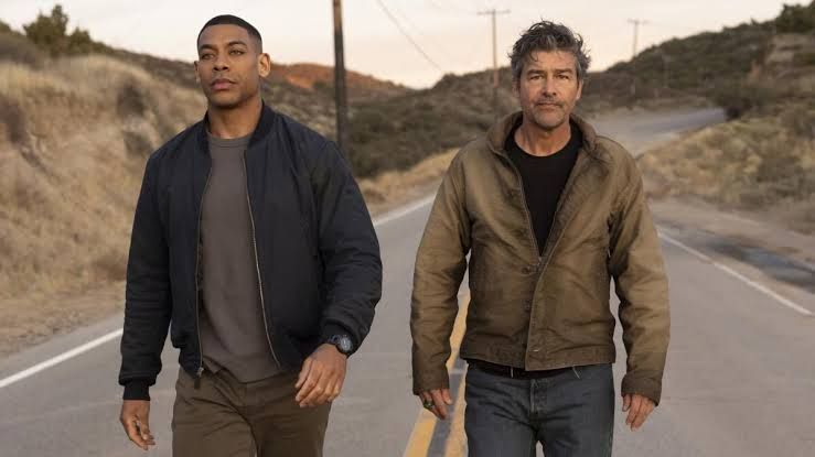 Kyle Chandler and Aaron Pierre stand in a rural field during their investigation in the HBO series Lanterns.