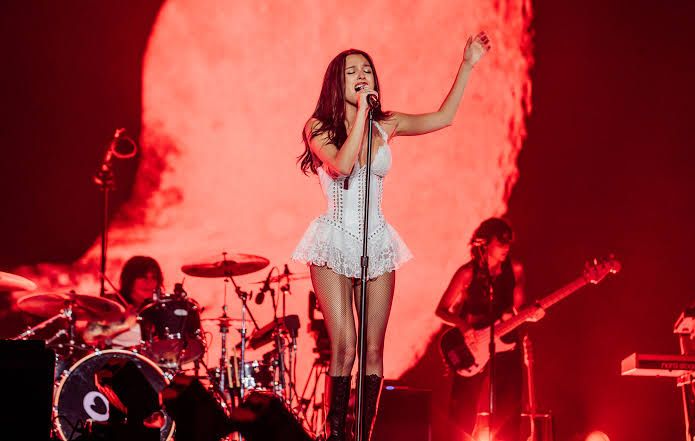 Olivia Rodrigo performing on stage during a recent concert, holding a microphone while singing.
