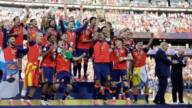 Spanish soccer players celebrate winning the World Cup trophy on the field while officials look on.