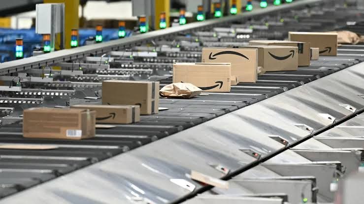 Amazon shipping packages moving on a conveyor belt in a large distribution facility.
