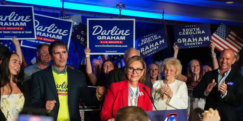 Sen. Darline Graham stands in front of a blue backdrop with her name, acknowledging supporters after her primary win.