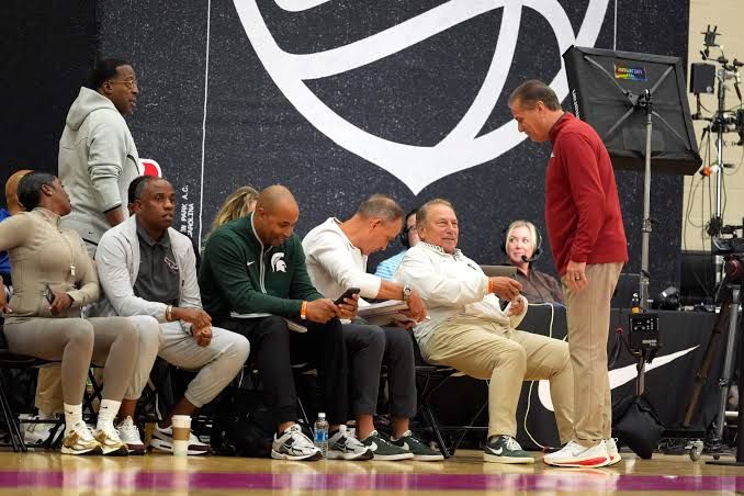 College basketball coaches observing practice from the sidelines at a summer recruitment event.