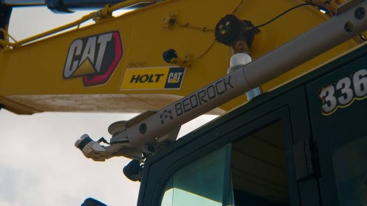 An autonomous excavator digging at a construction site with an empty cabin and sensors mounted on the exterior.